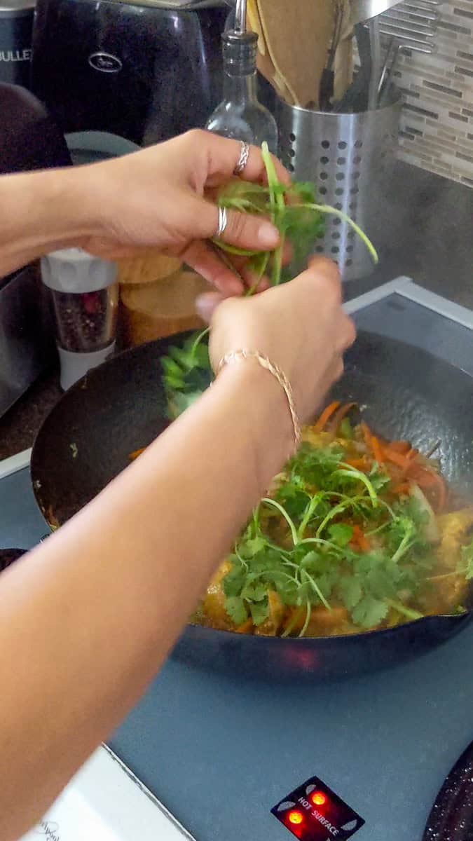 the simple jaimaican curry chicken being garnished with fresh cilantro sprigs.