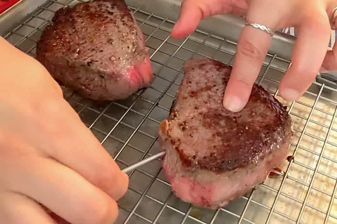 Meat thermometer checks medium-rare steak on a cooling rack in a cozy kitchen.