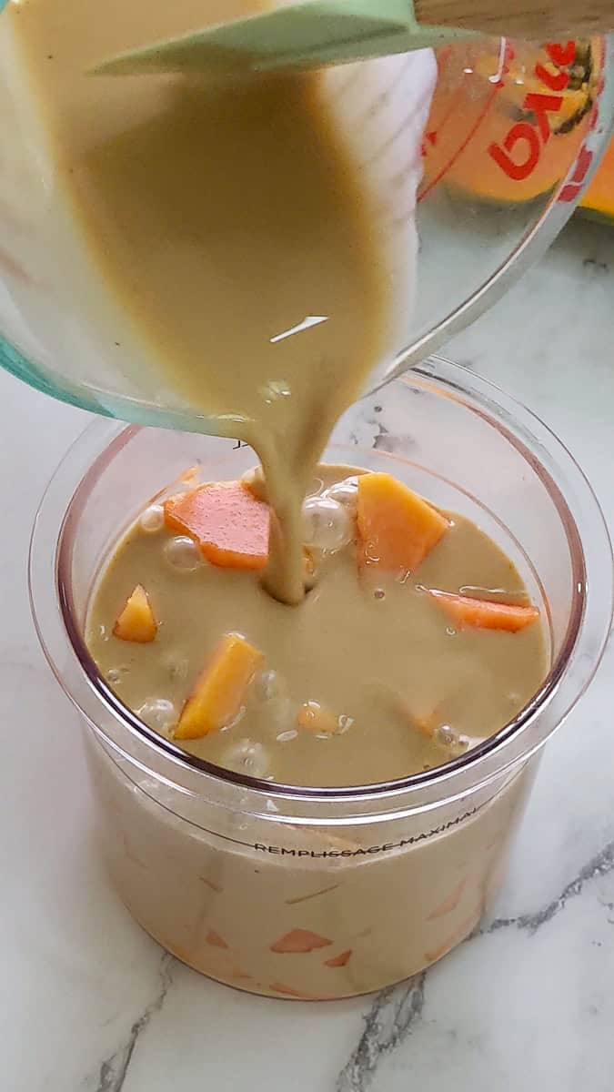 coconut cream rum mixture poured over papaya chunks in a ninja creami pint container.