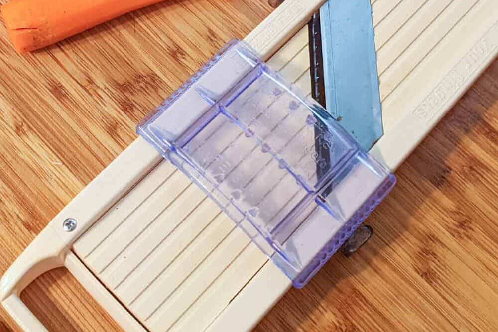 a japanese mandoline on a wooden cutting board with a hand guard.