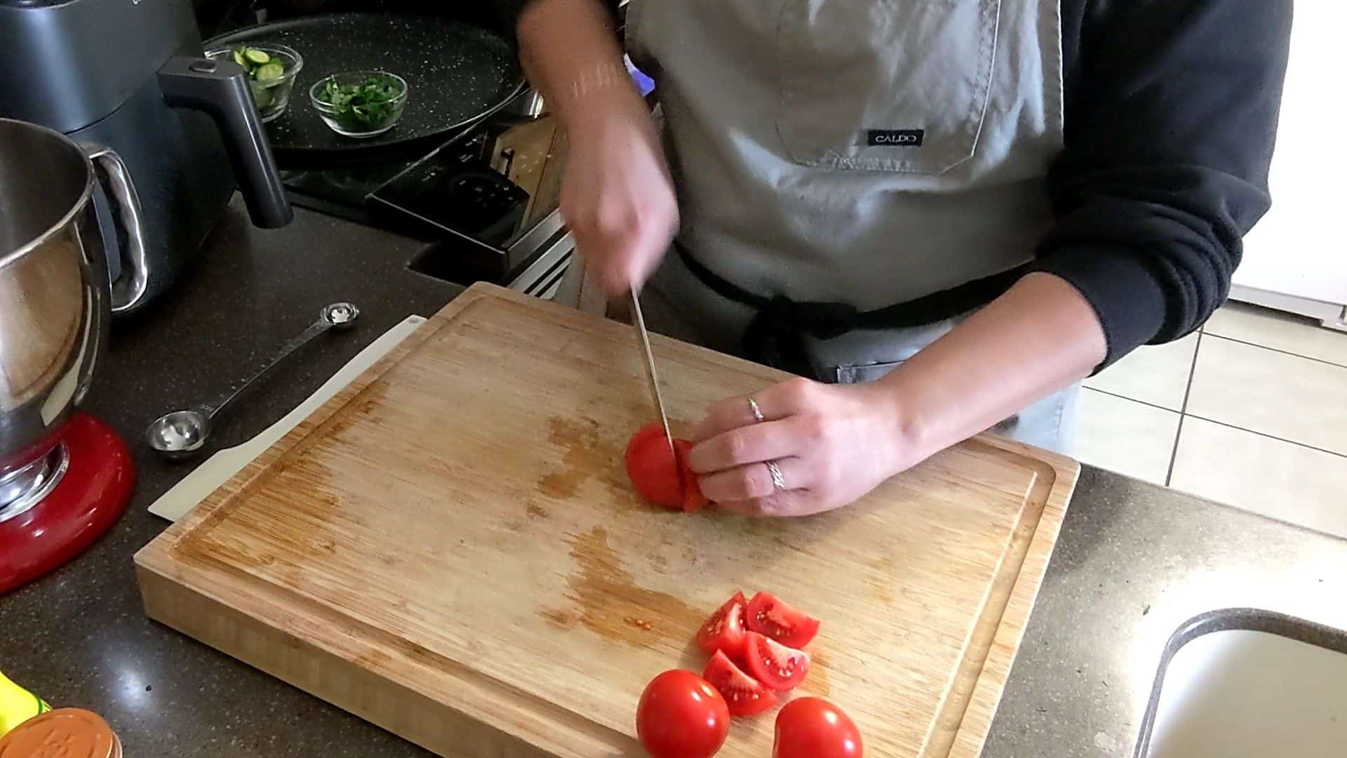 chef maika cutting tomatoes into quarters on a cutting board, a clip from a tutorial video.