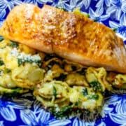Air fried salmon fillet served with spinach and tortellini pasta on a blue patterned plate.