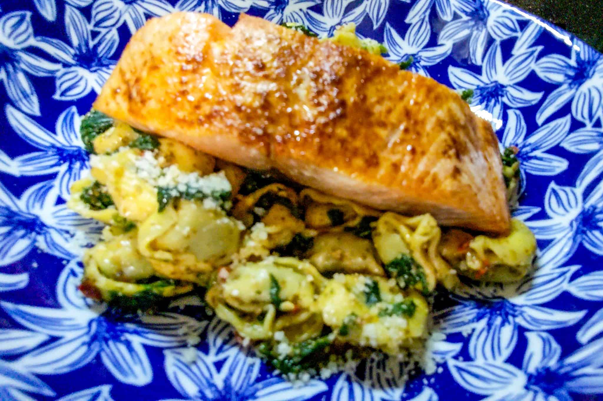 Air fried salmon fillet served with spinach and tortellini pasta on a blue patterned plate.