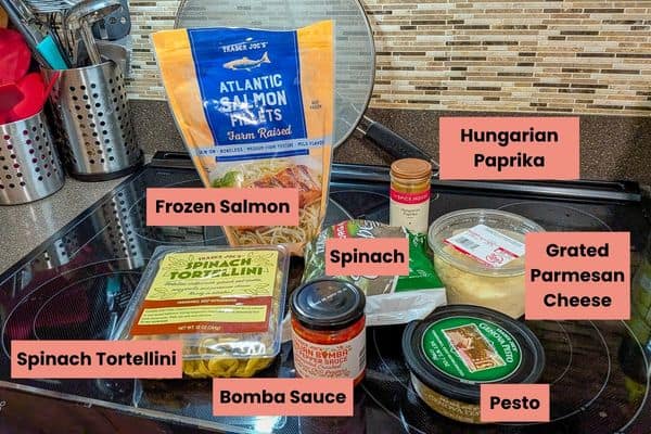 Frozen salmon, spinach, grated Parmesan, and pasta ingredients on kitchen counter.