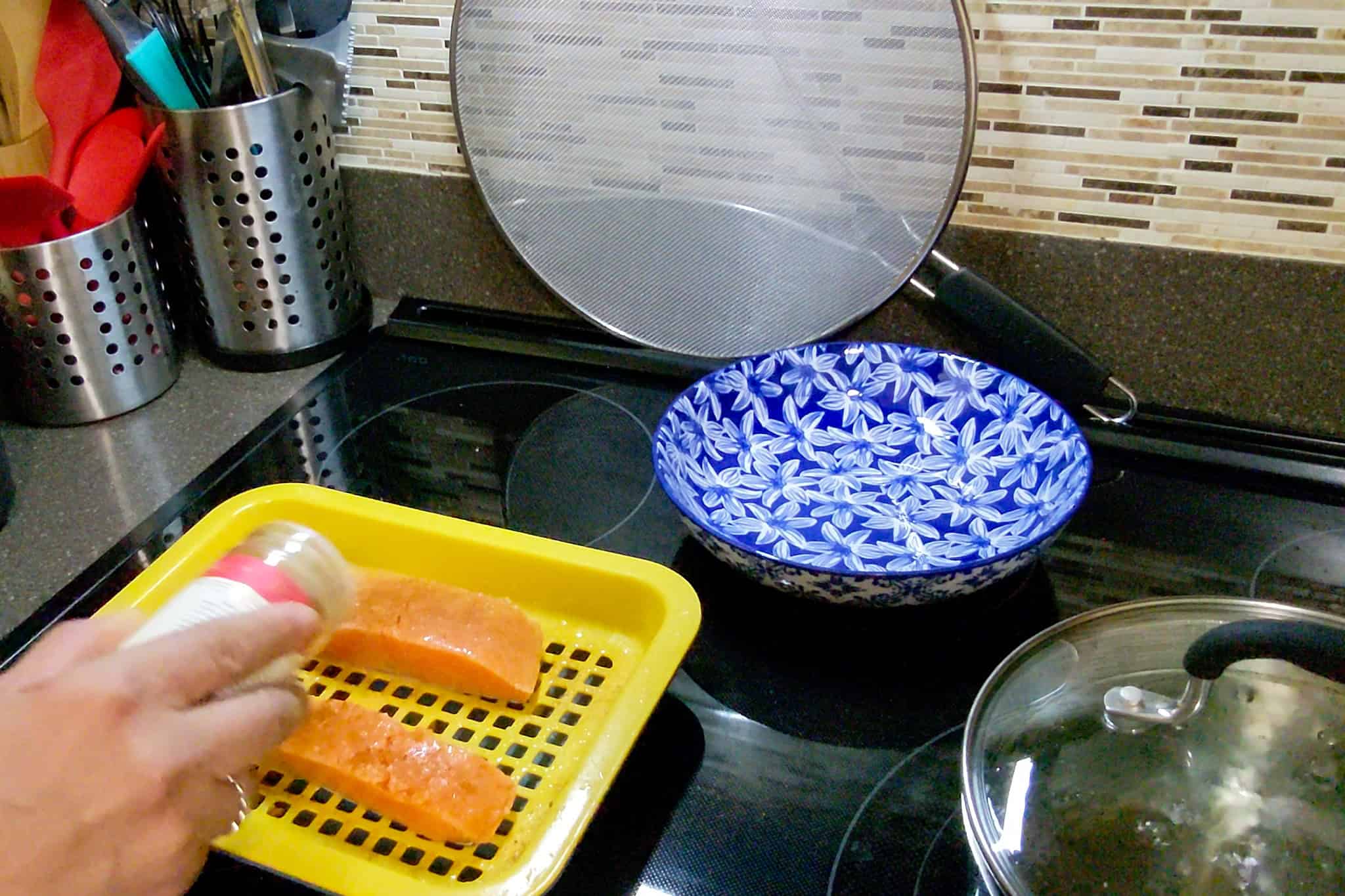Chef seasoning salmon fillets on a yellow tray in a kitchen.
