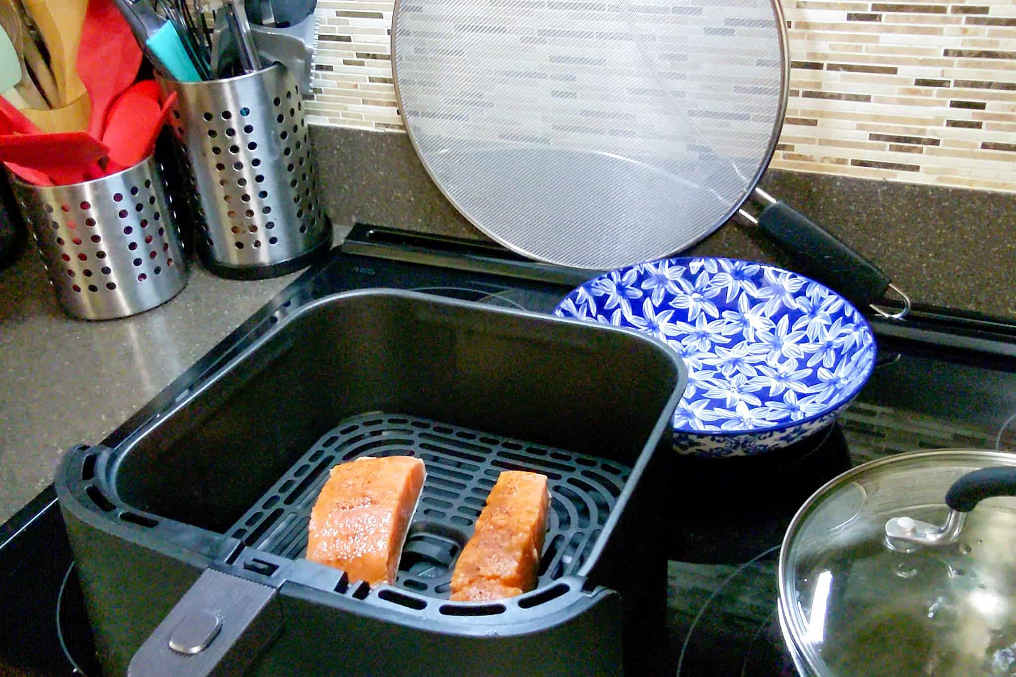Salmon fillets resting in a black air fryer basket on stove top.