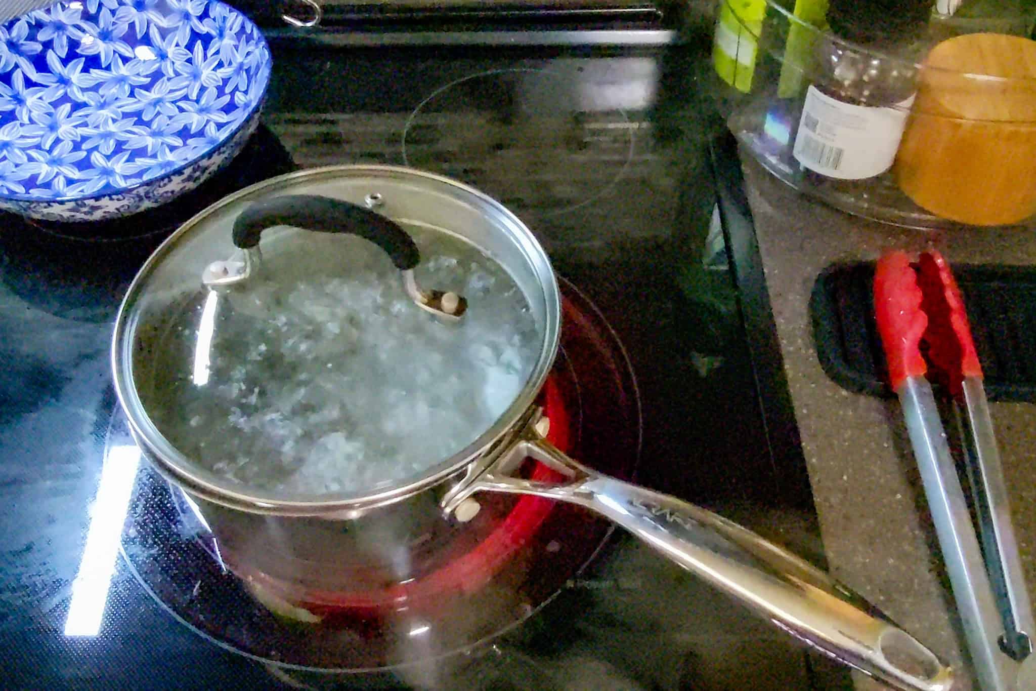 Pot of boiling water on stove with lid, kitchen setting.