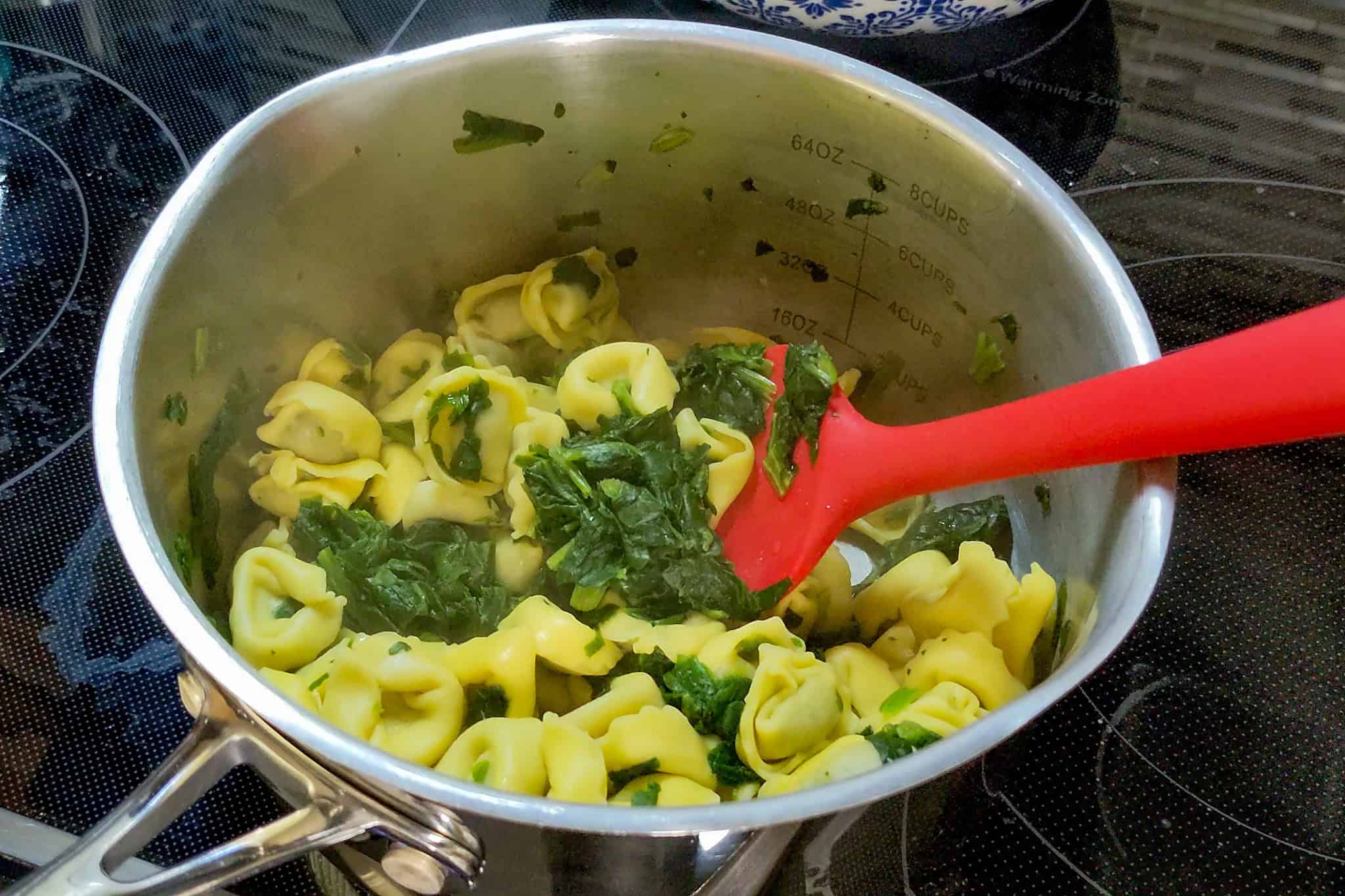 Tortellini pasta with spinach cooking in a pot on stove.