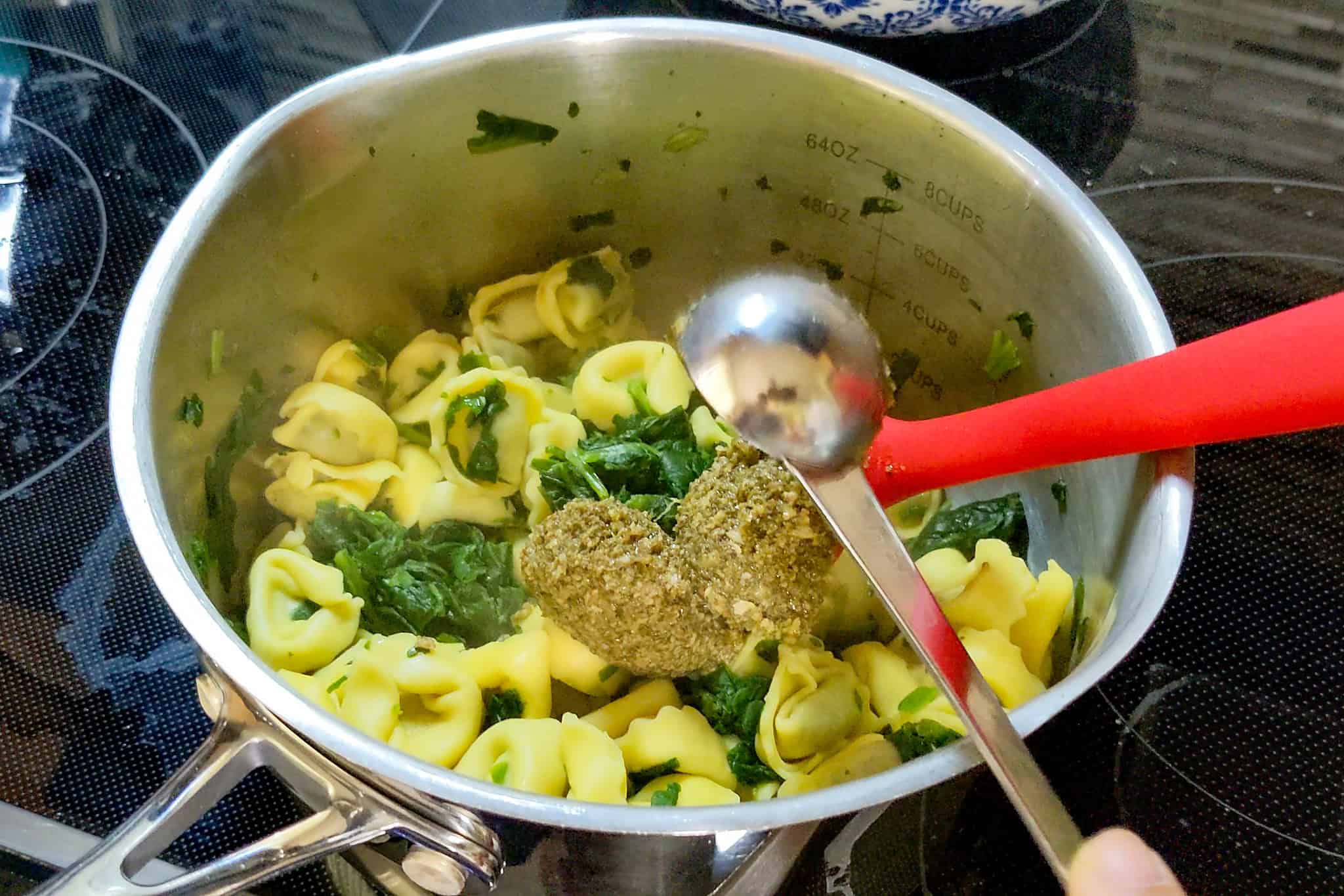 Tortellini pasta with spinach and pesto cooking in a pot on stove.
