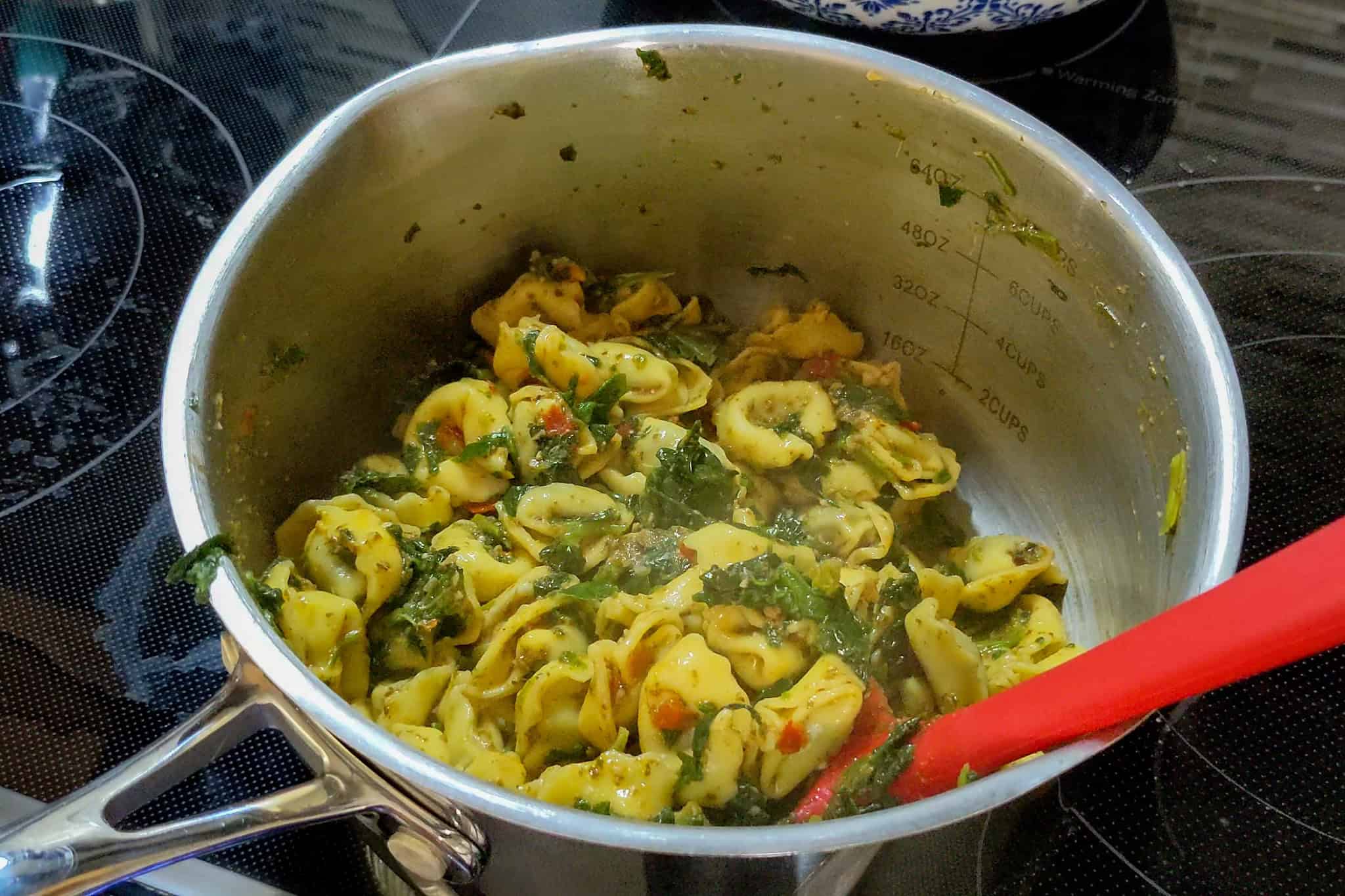 Cooking homemade tortellini with pesto in a stainless steel pot on stove.