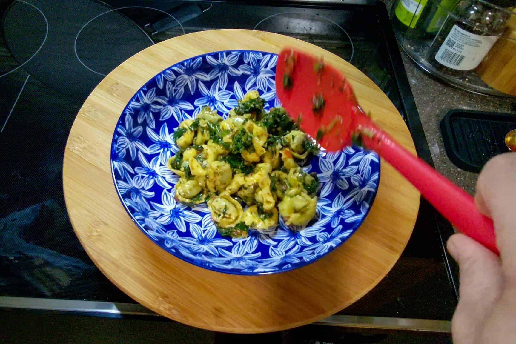 Fresh spinach tortellini pasta in a blue patterned bowl with a red spatula.