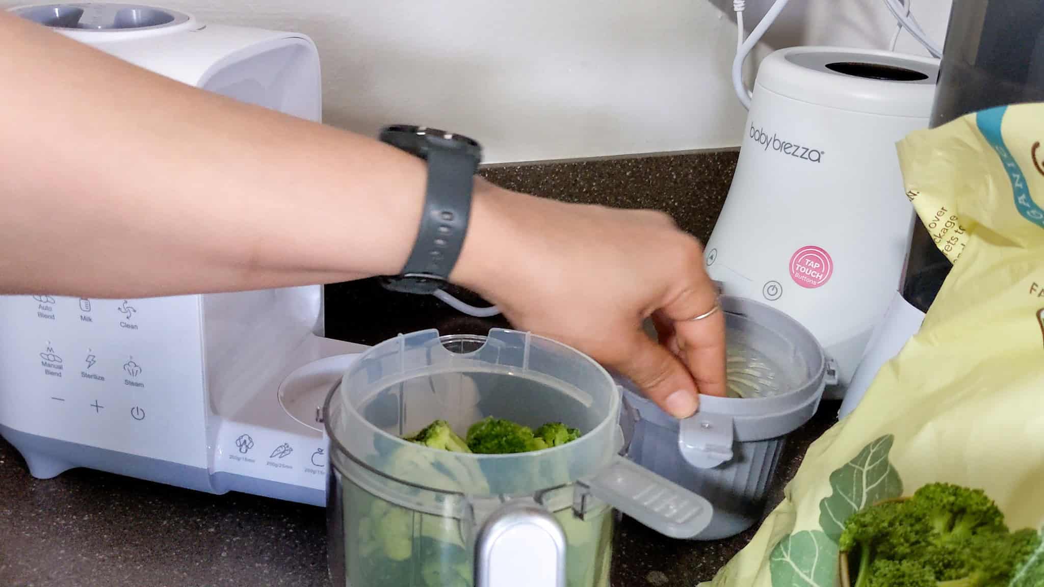 frozen broccoli florets placed in the bear baby food maker steam basket with a bag of organic frozen broccoli in the background.