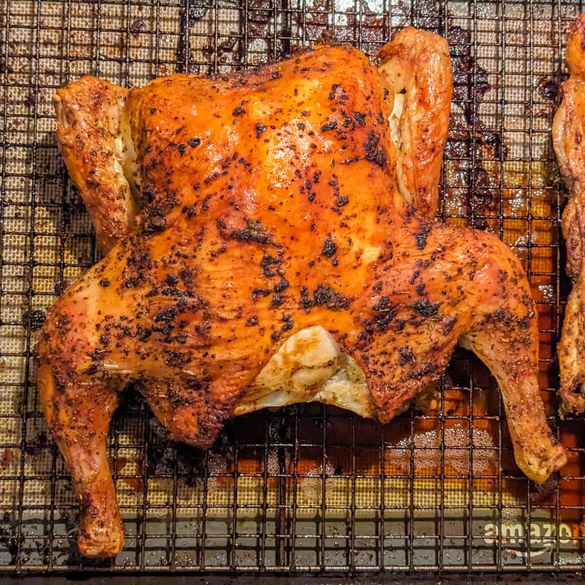 whole golden brown Roasted spatchcock chicken with backbone seperated and roasted as well on a sheet pan with a wire rack.