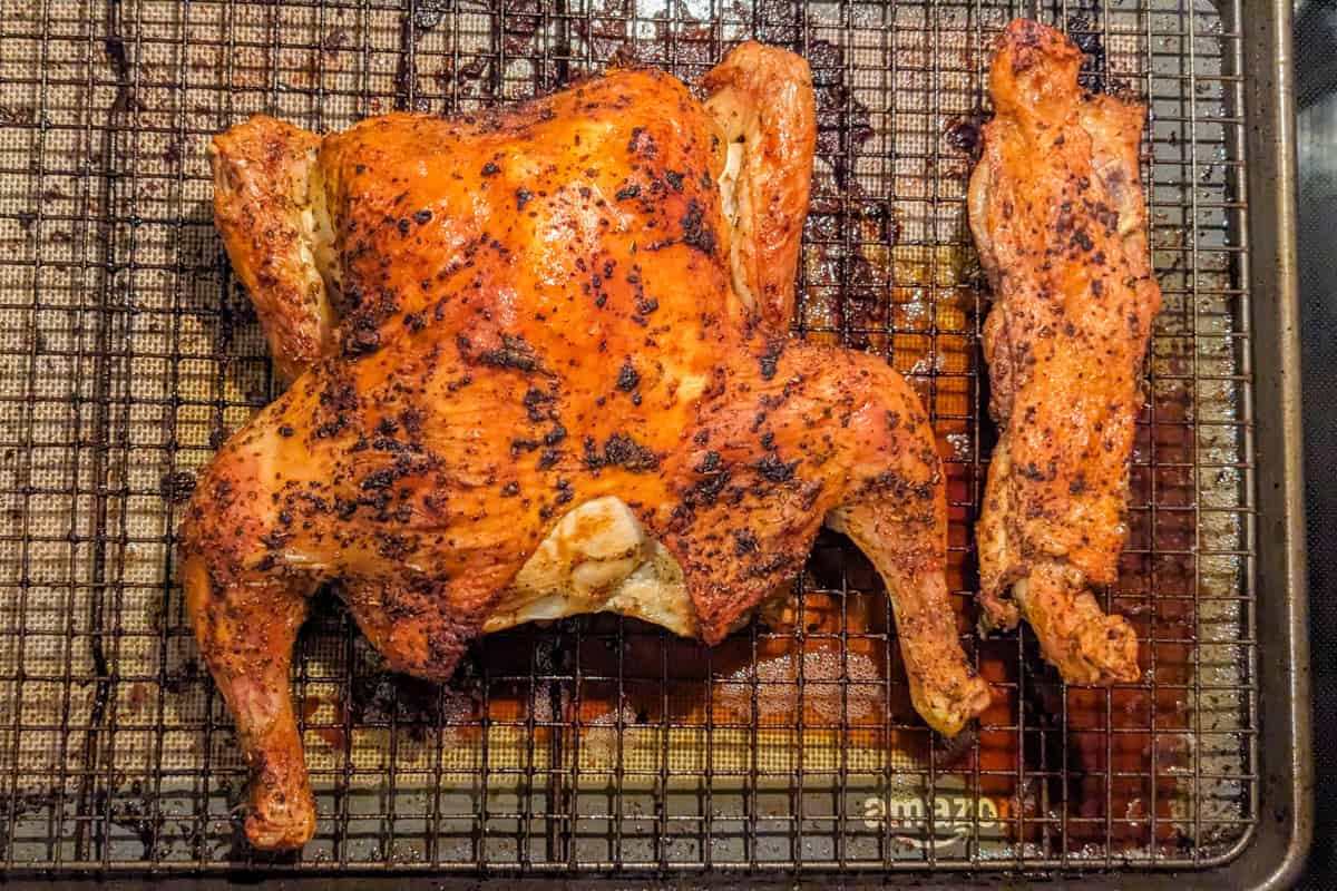 whole golden brown Roasted spatchcock chicken with backbone seperated and roasted as well on a sheet pan with a wire rack.