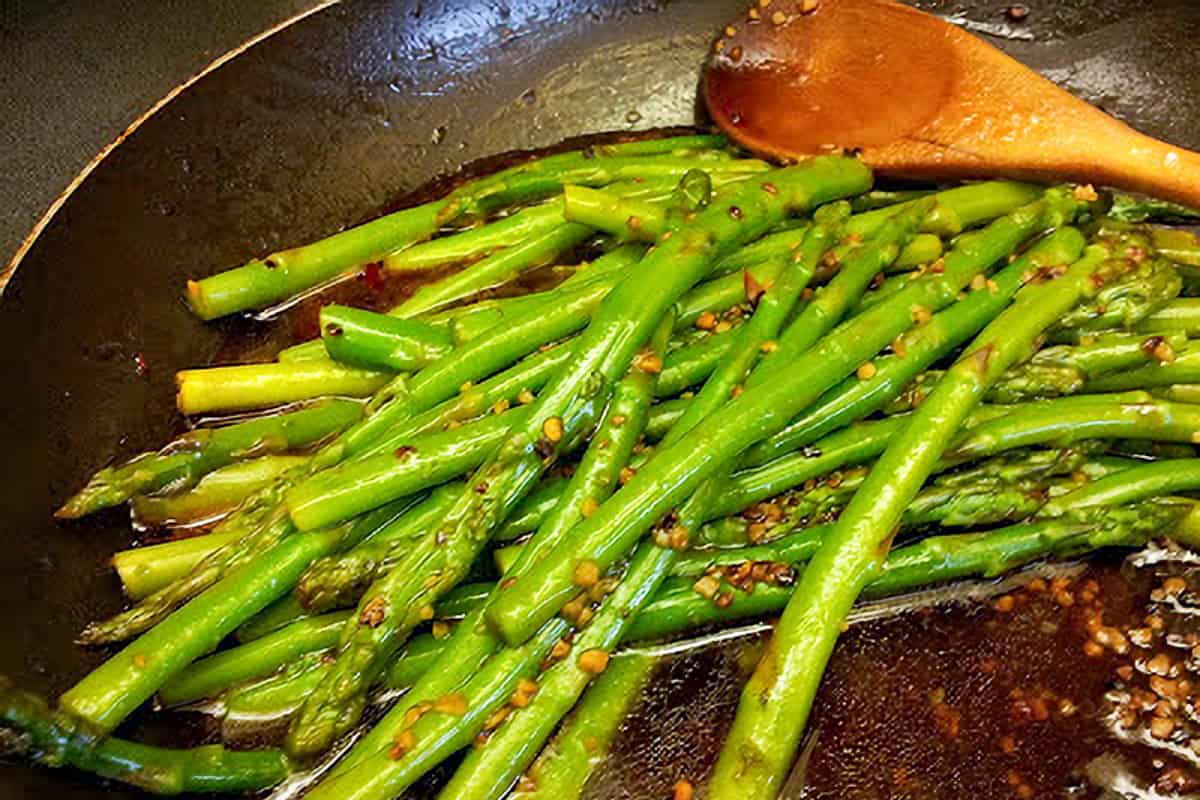 stir fried pencil asparagus in sauce in a non-stick frying pan.