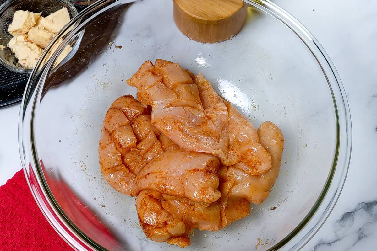Raw seasoned chicken breasts with shallow diamond cuts before air frying in a glass mixing bowl.
