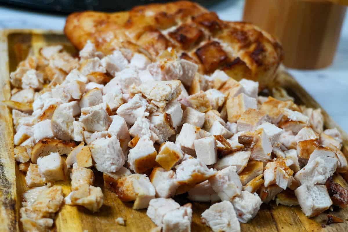 diced cooked chicken breast on a cutting board with a cooked diamond slit chicken in the background.