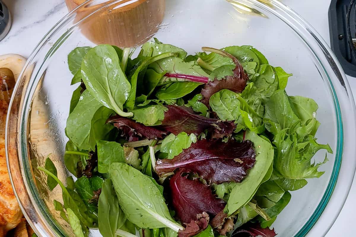 dressing mixed greens in a pyrex glass mixing bowl.