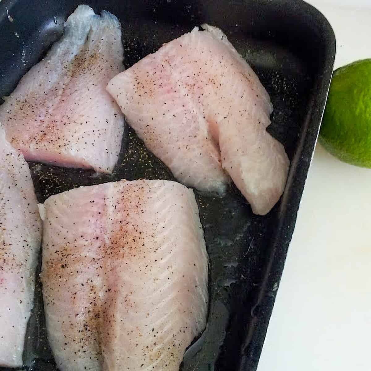 Raw basa fish fillets seasoned with black pepper before cooking.