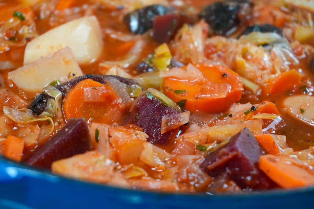 Finished bowl of hearty borscht with potatoes, carrots, cabbage, white beans, and beets.
