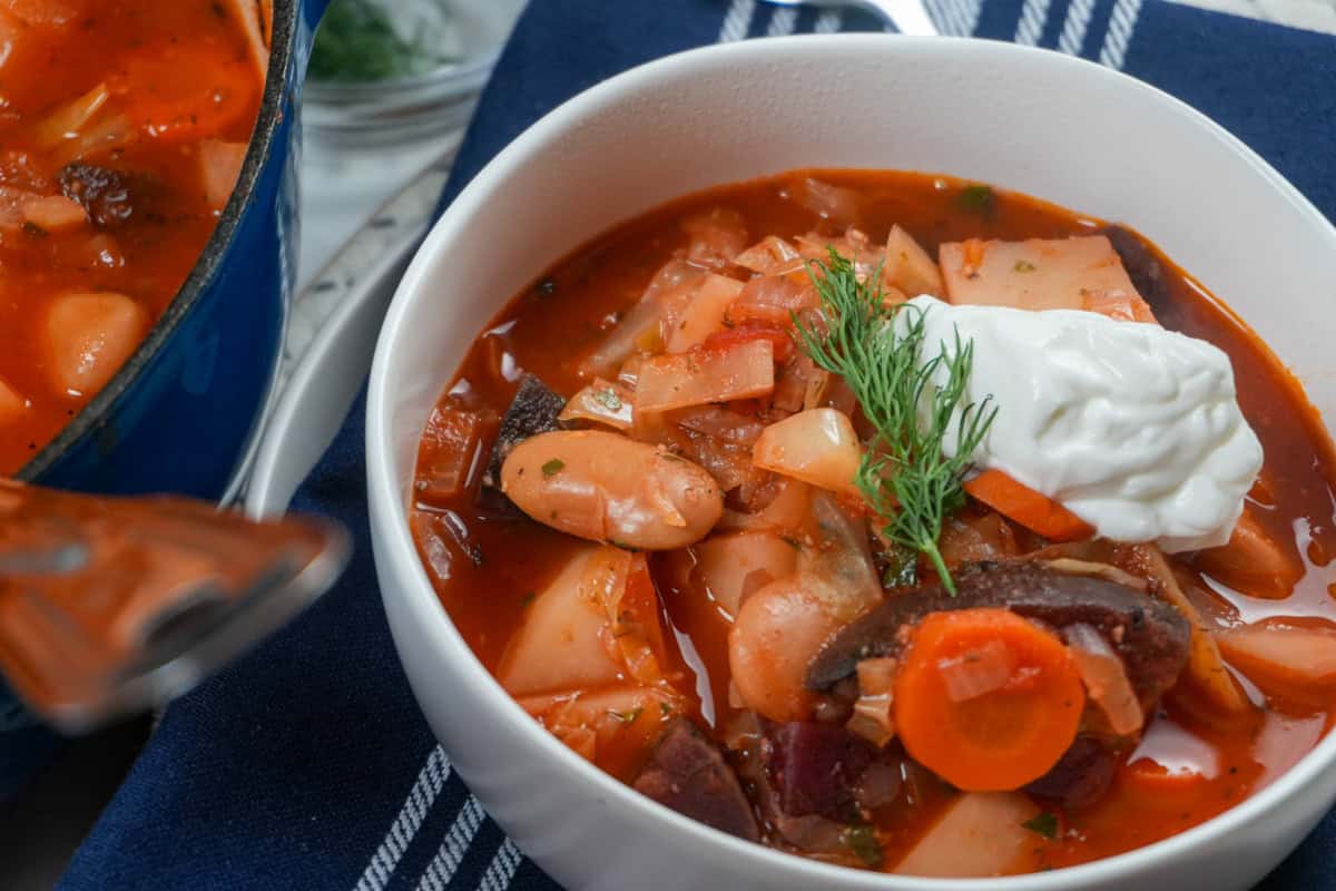 Homemade borscht served with sour cream and fresh dill beside a Dutch oven.