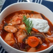 Homemade borscht served with sour cream and fresh dill beside a Dutch oven.