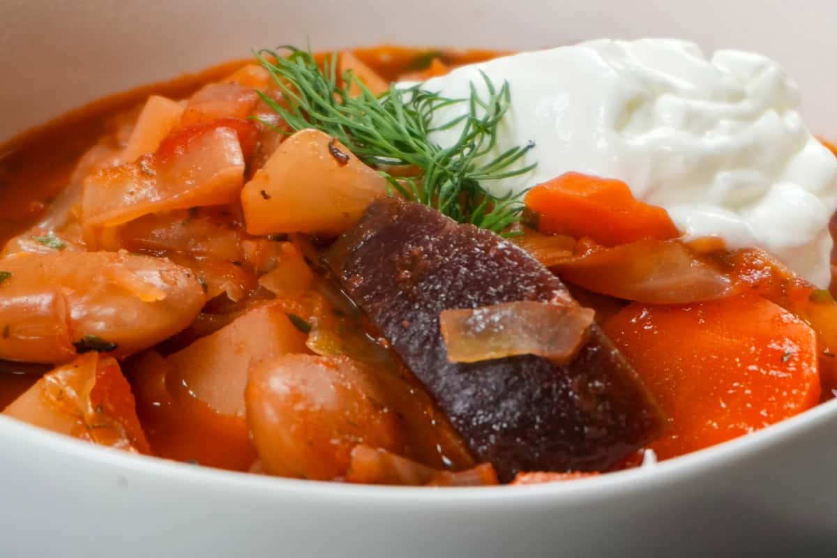 Easy borscht soup with vegetables, white beans, sour cream, and fresh dill in a white bowl.