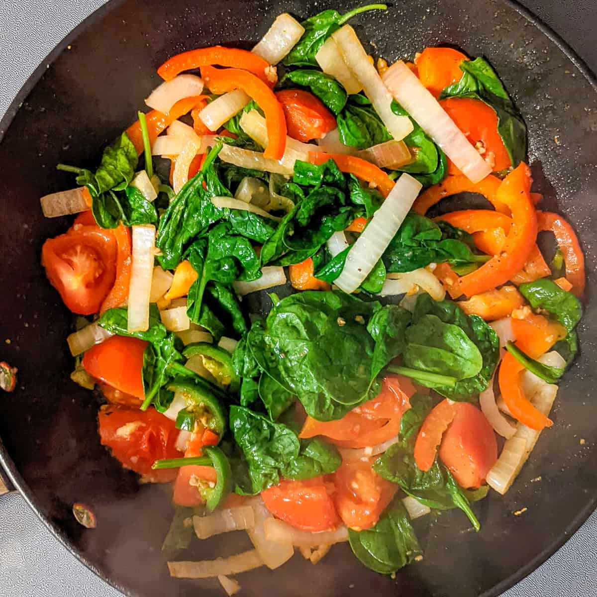 Sauted spinach, tomatoes, bell peppers and onion partially cooked in an all-clad non-stick saute pan.