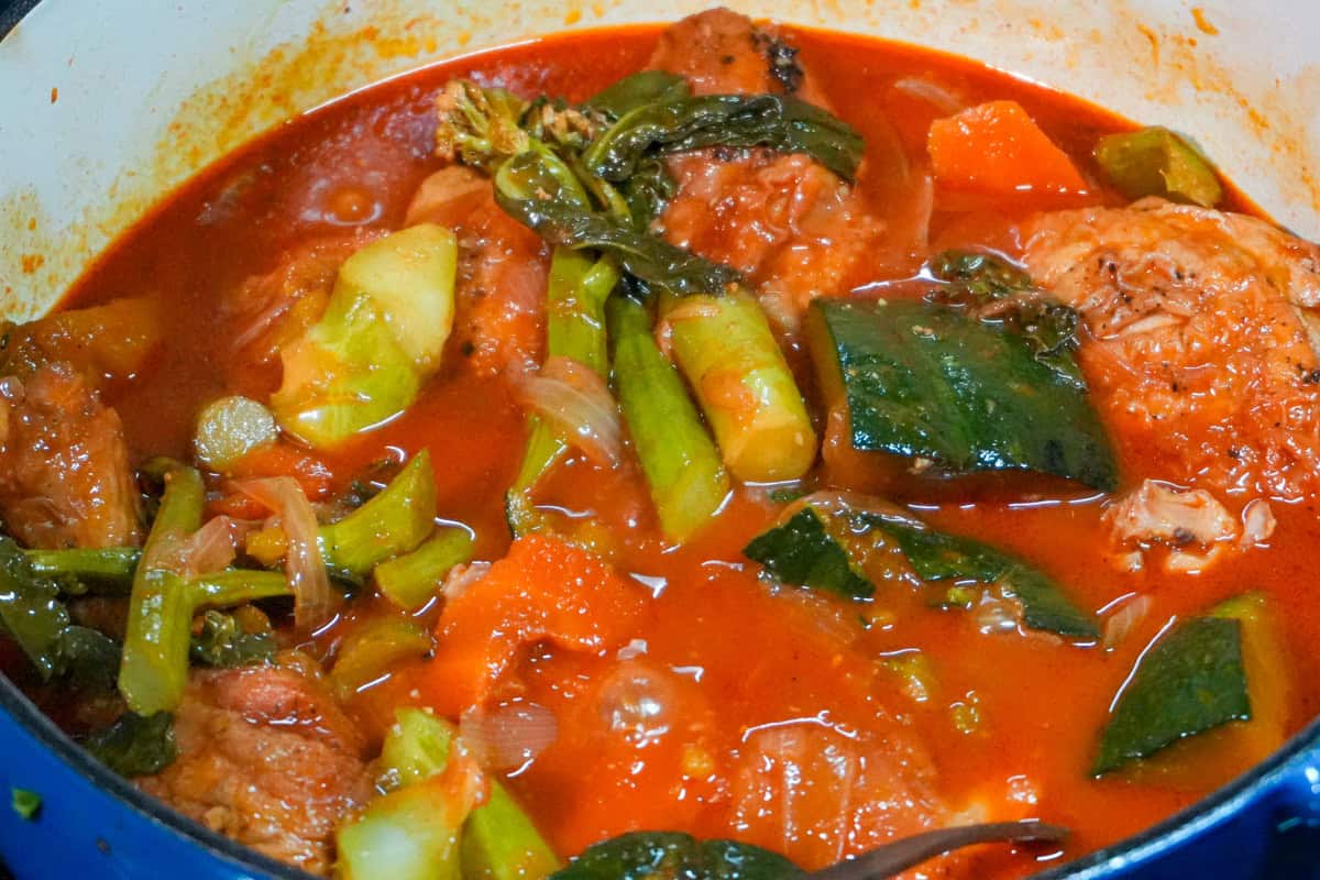 Bone-in chicken, kabocha, and carrots in red sauce in a dutch oven.