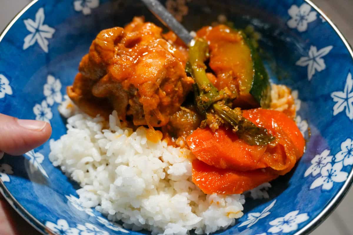 Bone-in chicken, kabocha, and carrots in red sauce beside a bowl of white rice.