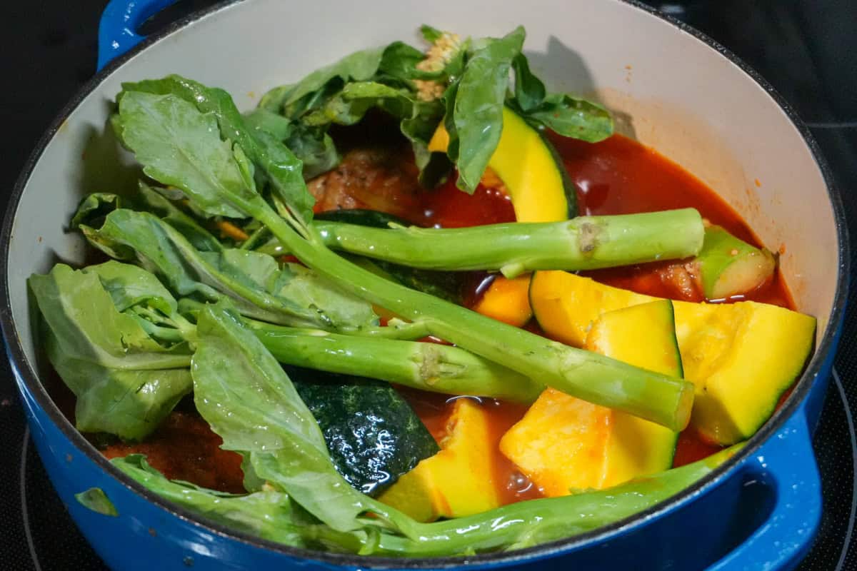 Whole yu choy sum resting over chicken and kabocha in a stew pot.