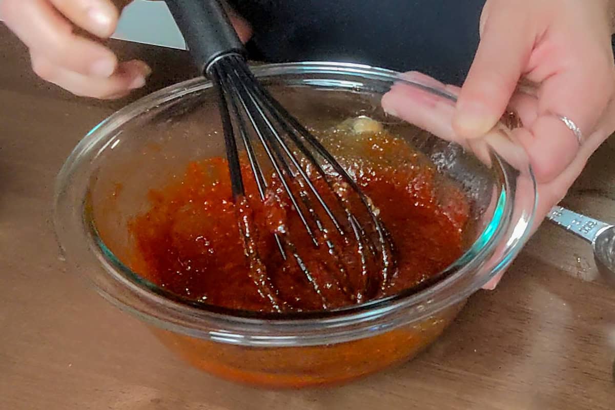 In a small glass bowl with a silicone black whisk, combined gochujang, gochugaru, soy sauce, optional oyster sauce, sweetener, jarred Korean garlic paste, jarred Korean ginger paste, sesame oil, and black pepper.