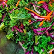 close up of massaged kale with strips of carrots, red radish and purple cabbage in a bowl.