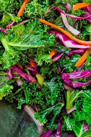 close up of massaged kale with strips of carrots, red radish and purple cabbage in a bowl.