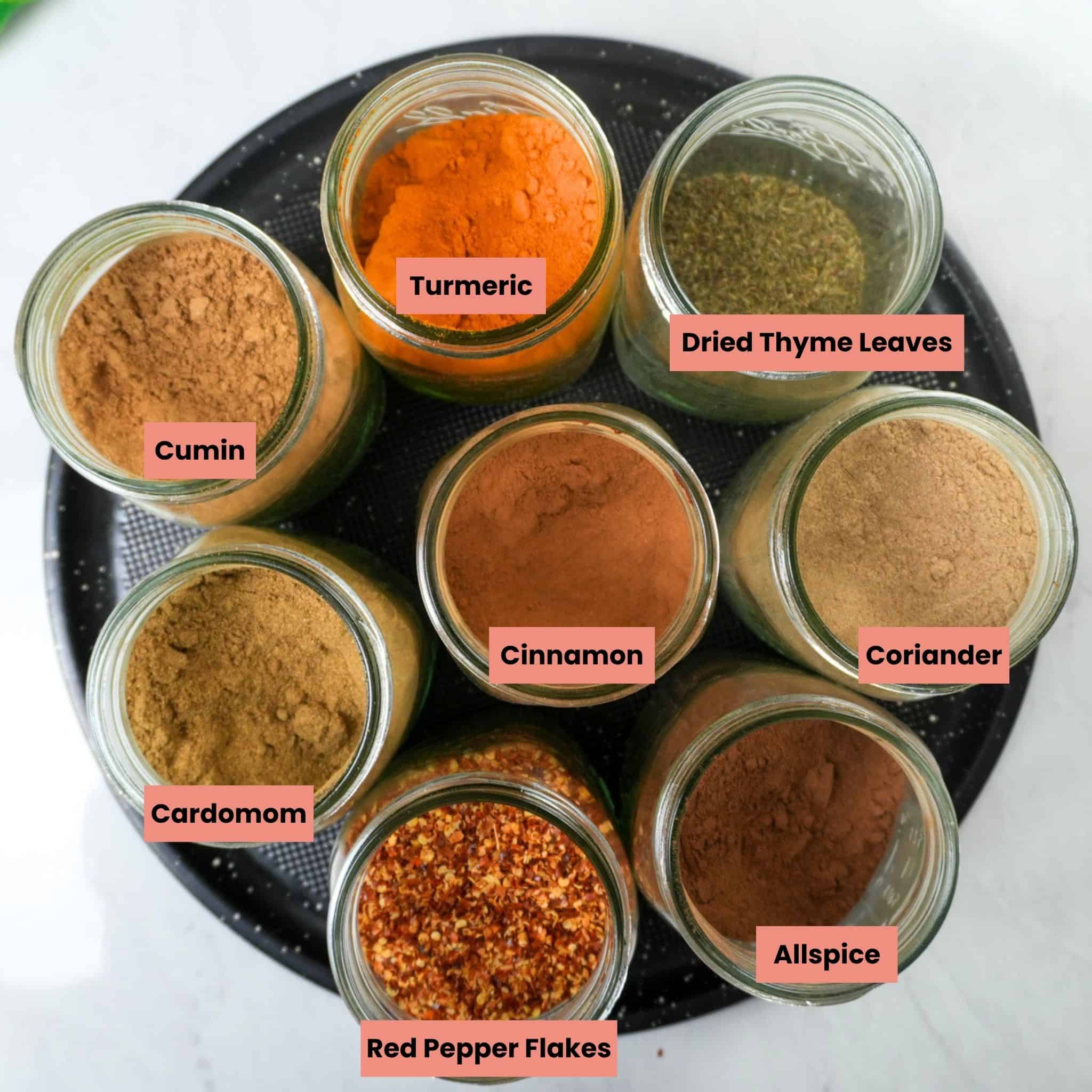 cumin, turmeric, dried thyme leaves, cinnamon, cardamom, coriander, allspice, and red pepper flakes in glass mason jars.