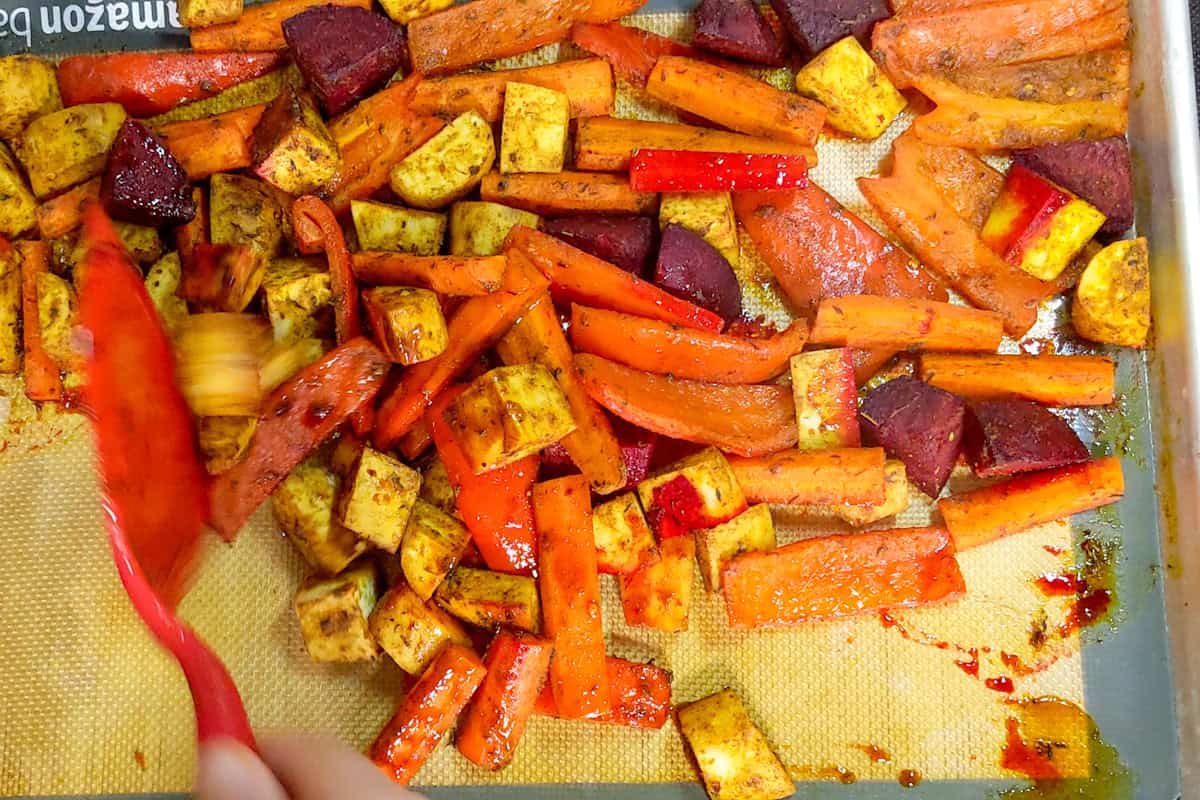 Roasted root vegetables with browned edges spread across a parchment-lined baking sheet.