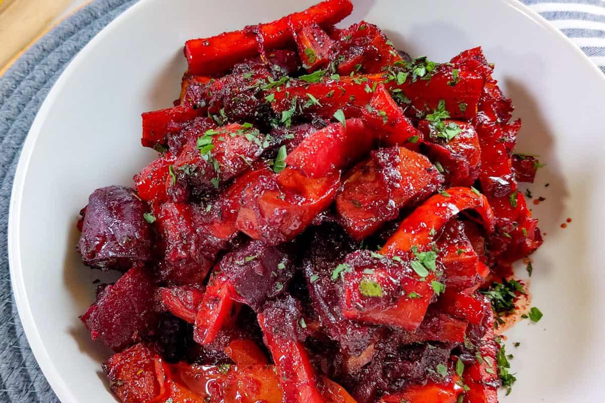 finished Roasted sweet potatoes, carrots, red peppers, and beets coated in a glossy red beet glaze in a large white serving bowl.