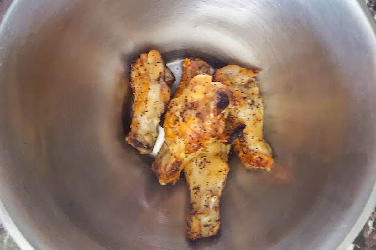 Browned chicken drumettes in a metal mixing bowl.