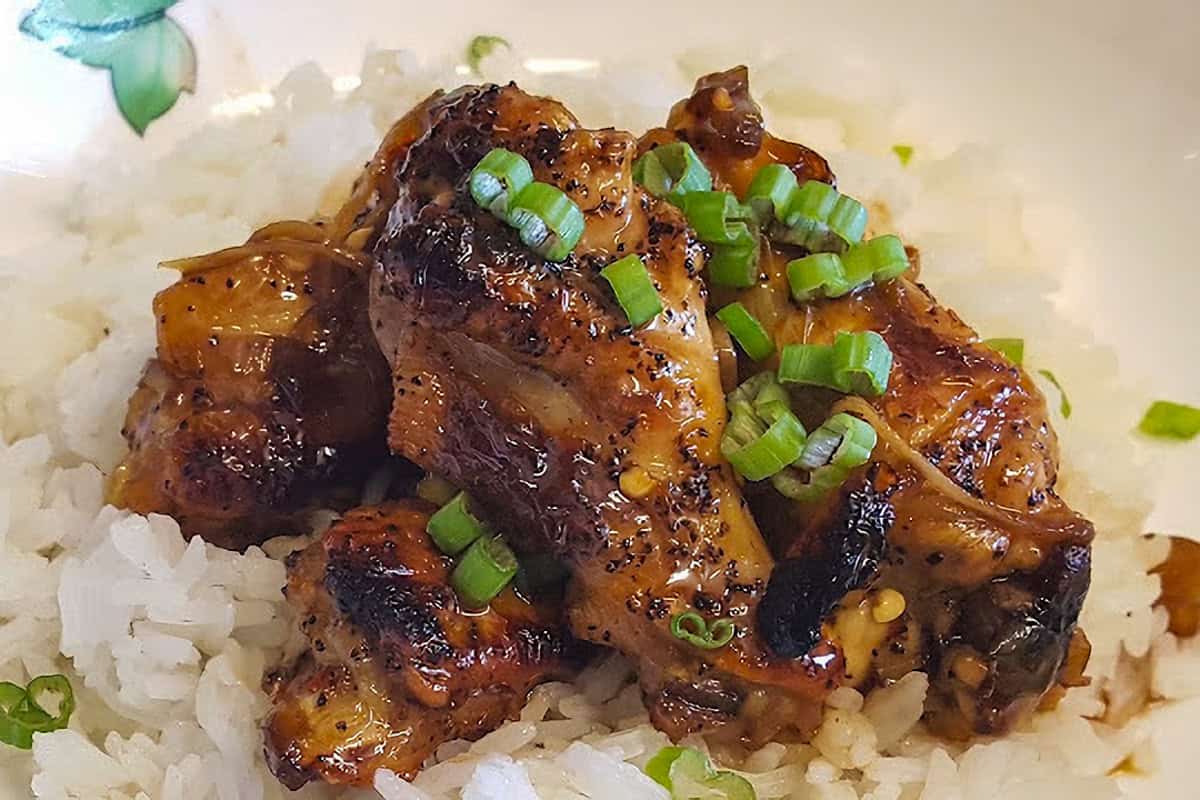 Chicken drumettes and sauce served over white rice in a shallow bowl.